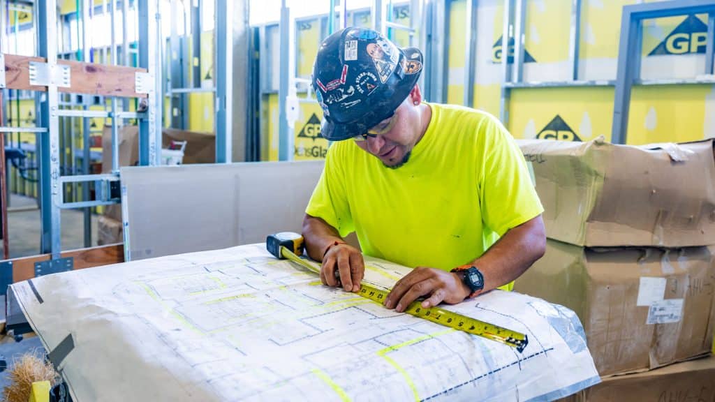 Man at construction site measuring diagrams on paper