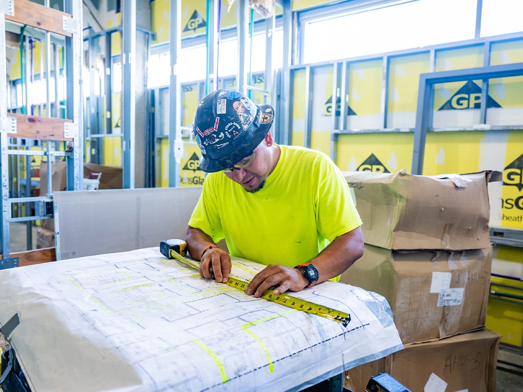 Man at construction site measuring diagrams on paper